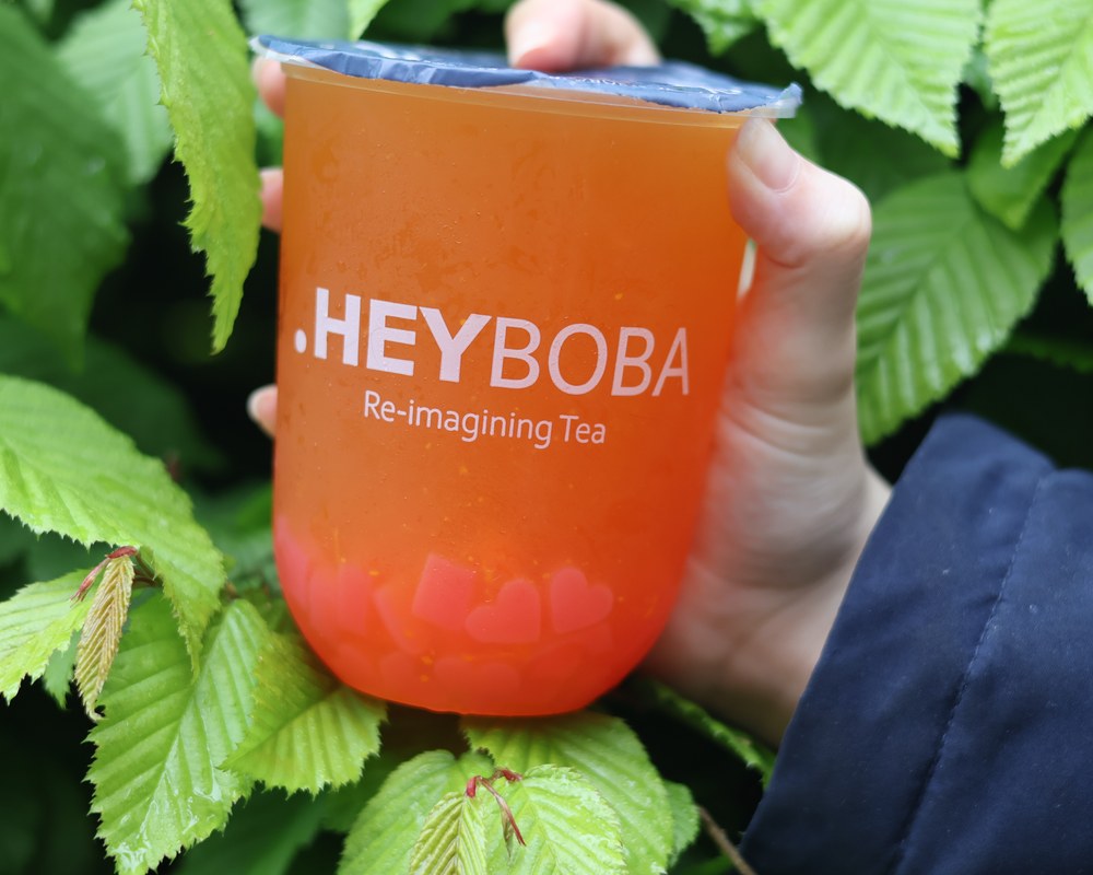 Orange HEYBOBA fruit tea held against green foliage