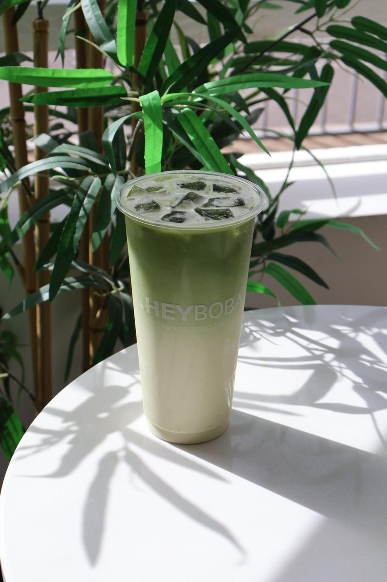 Layered iced HEYBOBA matcha beside green plants